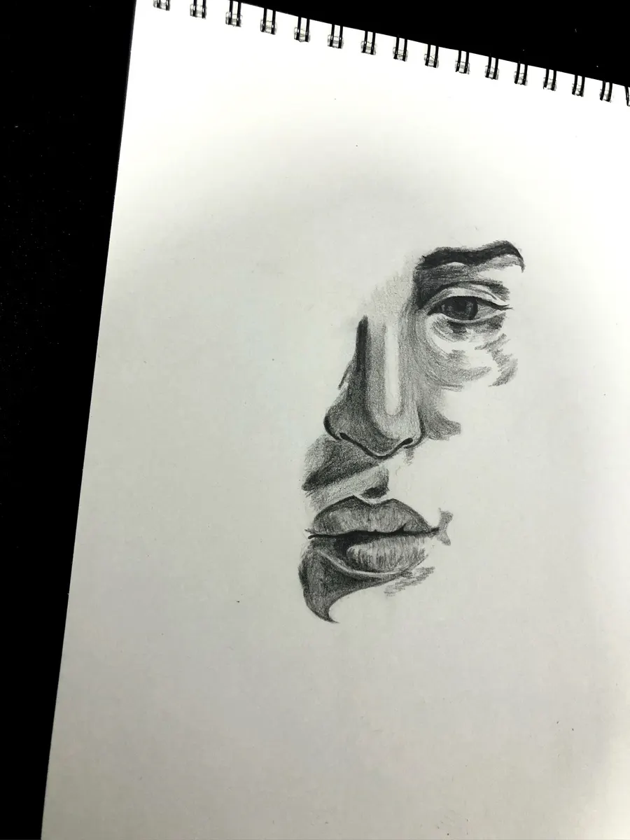 Boceto a lápiz de medio rostro, ojo, nariz y labios, en un cuaderno de espiral
