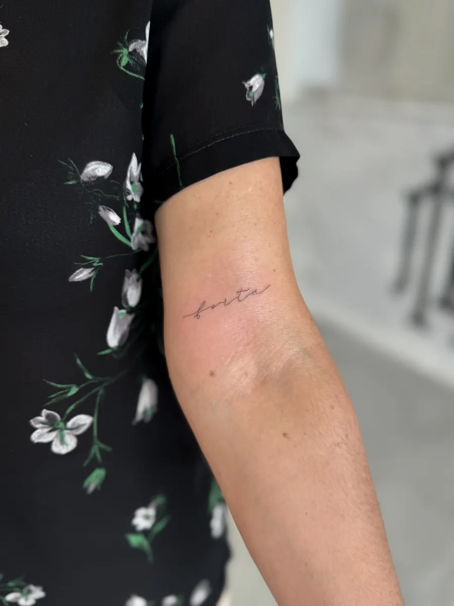 Palabra «forta» tatuada en cursiva de línea fina en el brazo