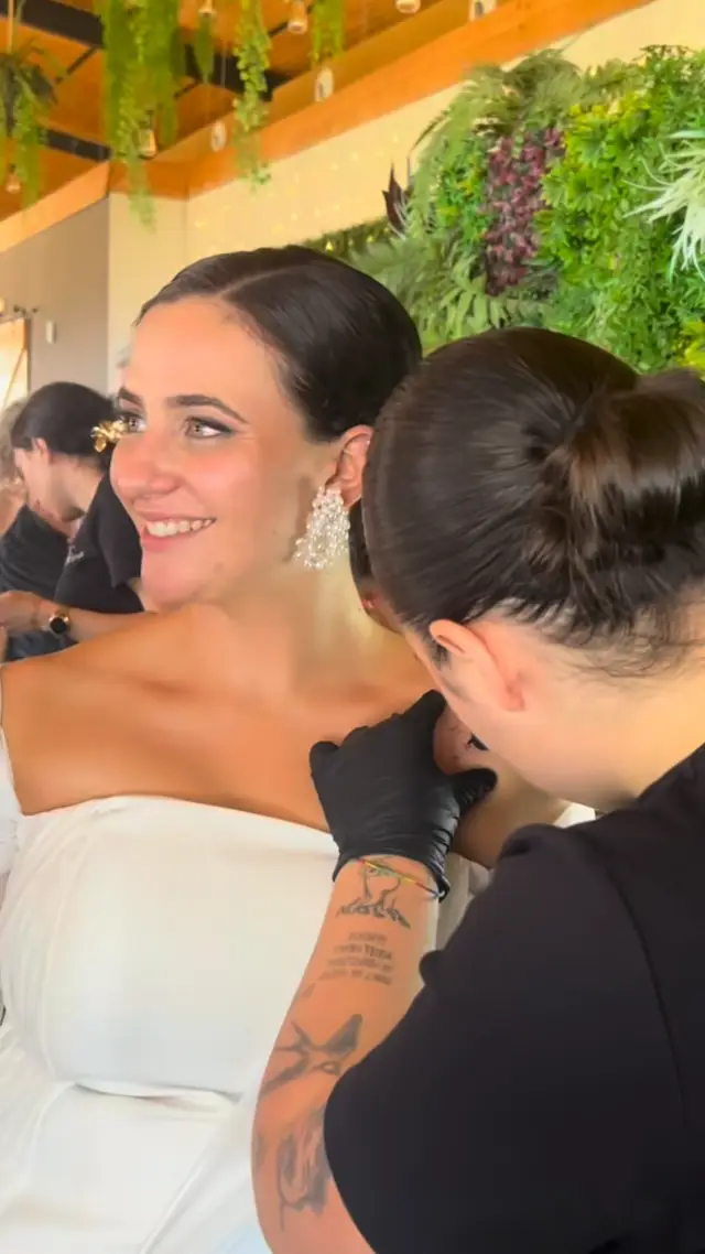 Alba tattooing a mini tattoo on a smiling bride's shoulder, one of her live illustrations of three guests, and Alba drawing at her table in a wedding garden