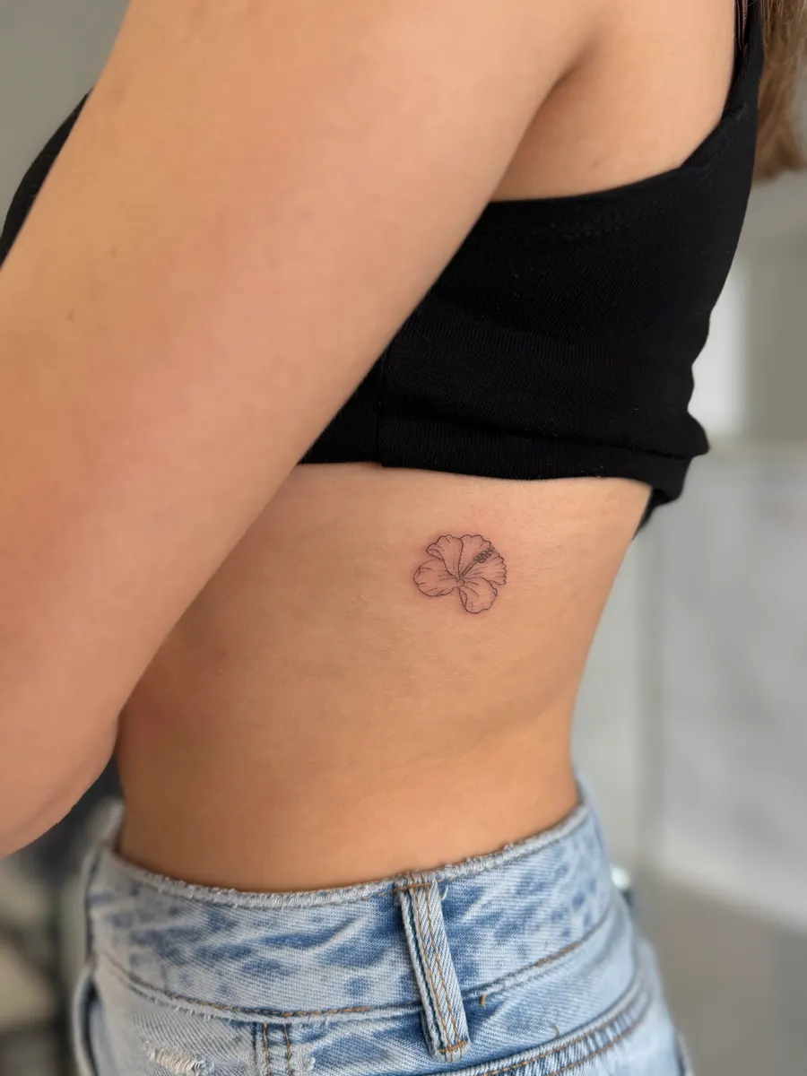 Small five-petal flower tattooed in fine line on the ribs